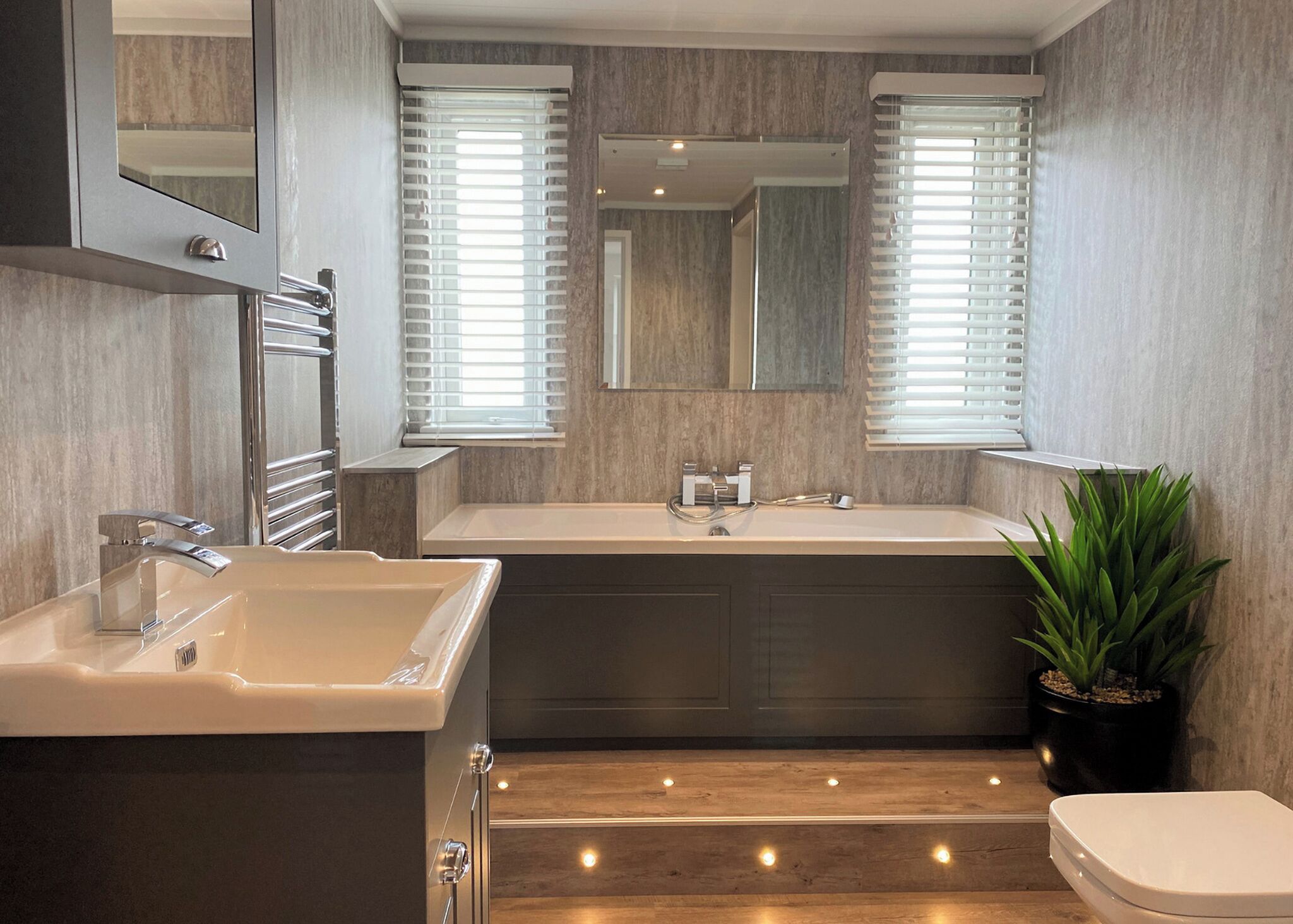 Une salle de bain moderne avec un grand lavabo, une baignoire, des toilettes et une plante en pot.