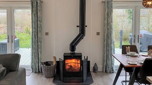 A cozy room with a wood-burning stove, a dining table set for two, and a view of the outdoors. - Experience the ultimate retreat in this stunning woodland lodge. (Chipping)