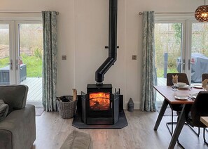 A cozy room with a wood-burning stove, a dining table set for two, and a view of the outdoors. - Experience the ultimate retreat in this stunning woodland lodge. (Chipping)