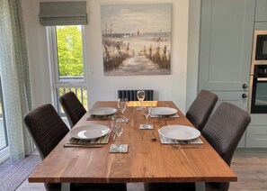 A dining table set for four with chairs, a painting above, and a view of greenery outside.