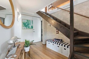Una escalera con barandilla de metal, un banco de madera con cojines a rayas, una planta en maceta y una lámpara de pared.