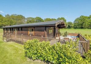 A wooden cabin with a deck, a hot tub, and a grassy yard. - Luxurious solid log lodge. (Wenhaston, Halesworth)