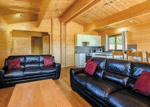 A cabin interior with two black leather sofas, wooden flooring, a kitchen area, and a dining table. - Luxurious solid log lodge. (Wenhaston, Halesworth)