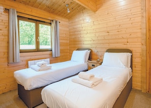 A cabin with two single beds, a nightstand, a lamp, and a window with curtains. - Luxurious solid log lodge. (Wenhaston, Halesworth)