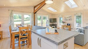A spacious kitchen with a central island, wooden dining table, and chairs, a living area with a sofa, and a TV. - Luxurious lodge with stunning countryside views. (Ashover)