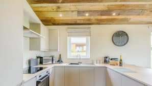 Una cocina moderna con armarios blancos, techo de madera, un ventanal grande y un reloj de pared.