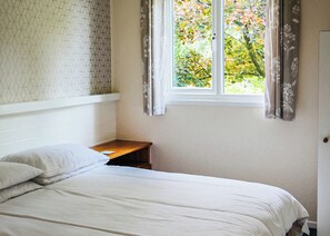 Une chambre à coucher comprenant un lit, une table de chevet, une fenêtre avec des rideaux et un mur orné d’un motif géométrique.
