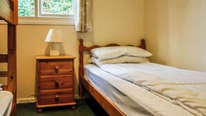 A single bed with a wooden frame, a bedside table with a lamp, and a window with curtains.