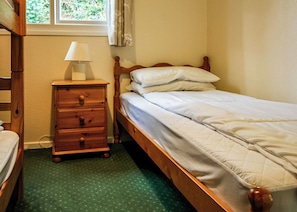Un lit simple avec un cadre en bois, une table de chevet avec une lampe et une fenêtre avec des rideaux.