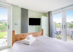 Ein Schlafzimmer mit einem Bett, einem an der Wand montierten Fernseher und einer Glasschiebetür, die zu einem Außenbereich mit Terrasse führt.