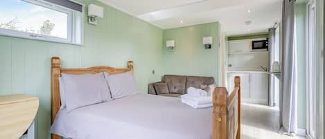 Un dormitorio con cama, escritorio de madera, sofá, microondas y vistas al exterior.