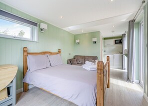 Ein Schlafzimmer mit Bett, Schreibtisch aus Holz, einer Couch, einer Mikrowelle und Blick ins Freie.