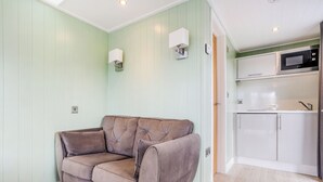 A room with a light green wall, a brown sofa, a white cabinet, and a microwave in the kitchen area.