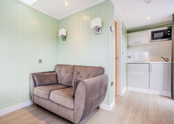 A room with a light green wall, a brown sofa, a white cabinet, and a microwave in the kitchen area.