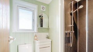 A bathroom with a toilet, sink, mirror, and shower.