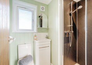 A bathroom with a toilet, sink, mirror, and shower.
