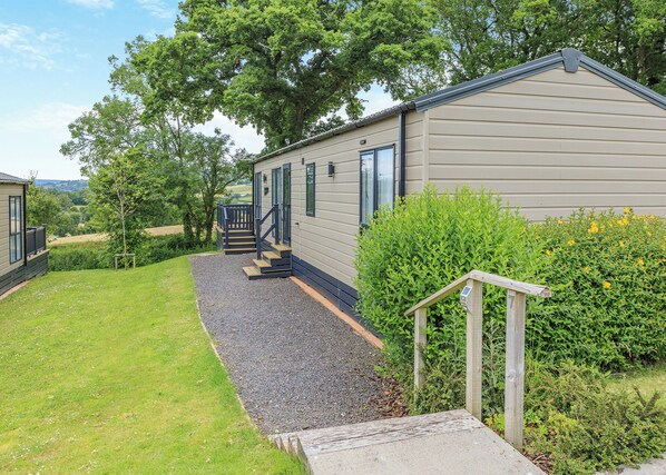 En etplans mobilhome med grusindkørsel, en trætrappe og en lille veranda.