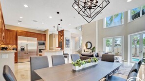 A modern kitchen with stainless steel appliances, a dining area with a large table and chairs, and a view of a pool through the glass doors. - The Nia Tower Ultimate Beach House (Pompano Beach)