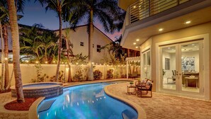 A swimming pool with a tiled deck, surrounded by palm trees and a patio area with outdoor furniture. - The Nia Tower Ultimate Beach House (Pompano Beach)