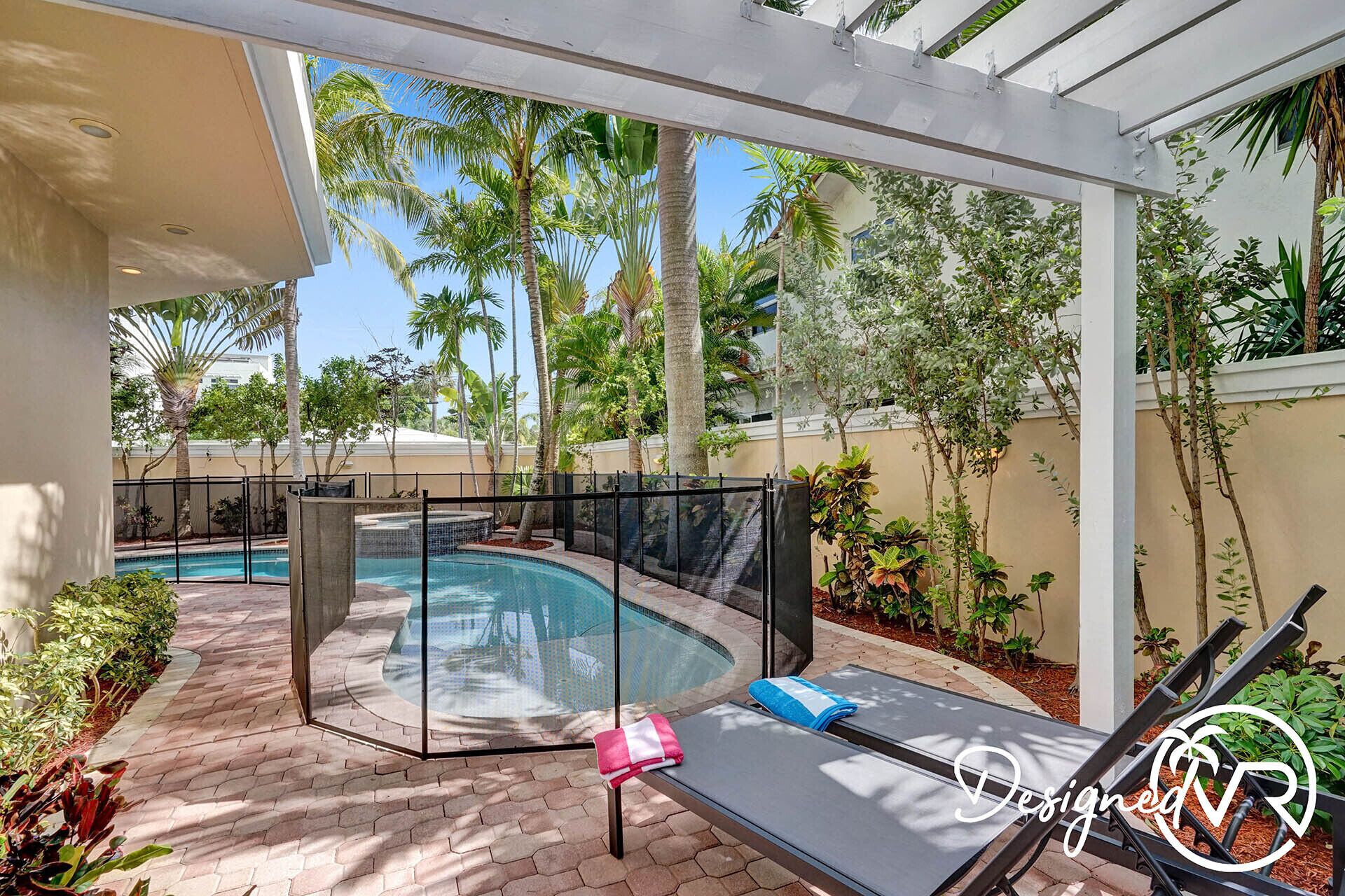 A pool area with a glass-enclosed section, lounge chairs, and a pergola.