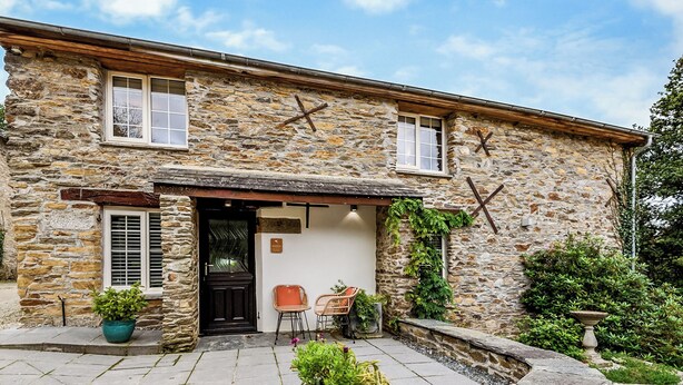 A stone building with a front door, two windows, and a small outdoor seating area with chairs and a table. - 1 bedroom accommodation in Watergate, Looe (Watergate, Looe)