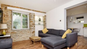 A modern living room with a stone wall, grey sofa, wooden flooring, and a dining area with a green countertop. - 1 bedroom accommodation in Watergate, Looe (Watergate, Looe)