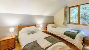 A bedroom with two wooden beds, a nightstand with a lamp, a window with curtains, and a radiator.