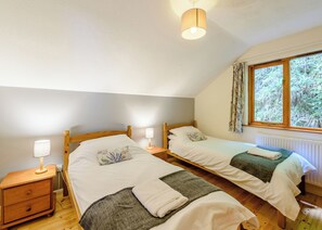 Ein Schlafzimmer mit zwei Holzbetten, einem Nachttisch mit Lampe, einem Fenster mit Vorhängen und einem Heizkörper.