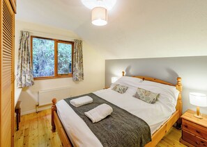 Une chambre à coucher avec un lit en bois, deux tables de chevet, un radiateur, une fenêtre avec des rideaux et un luminaire au plafond.