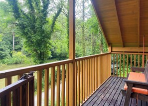Une terrasse en bois dotée d’une balustrade, qui offre une vue sur une rivière et est entourée d’une végétation luxuriante.