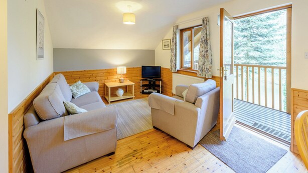A cozy living room with a wooden floor, two sofas, a TV, and a window with curtains. - Timber lodge set by the lake with one double and one twin. (Webbery, Bideford)