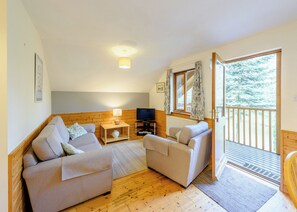 Ein gemütliches Wohnzimmer mit Holzboden, zwei Sofas, einem Fernseher und einem Fenster mit Vorhängen.