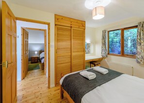 A bedroom with a wooden wardrobe, a bed with towels, a desk, a window with curtains, and a radiator. - Timber lodge set by the lake with one double and one twin. (Webbery, Bideford)