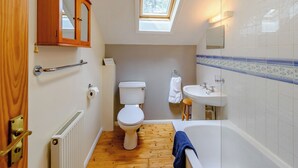 A bathroom with a toilet, sink, and bathtub, wooden flooring, a skylight, and a wooden door. - Timber lodge set by the lake with one double and one twin. (Webbery, Bideford)