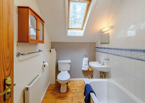 Une salle de bain comprenant des toilettes, un lavabo et une baignoire, un plancher en bois, un puits de lumière et une porte en bois.