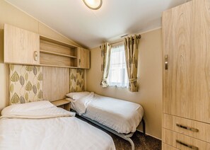 A bedroom with two beds, a wardrobe, and a window with curtains.