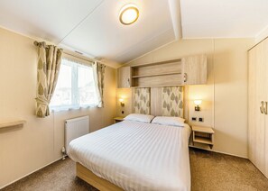 Un dormitorio con cama, mesitas de noche, radiador, ventana con cortinas e iluminación en la pared.