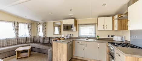 A compact kitchen with a microwave, sink, stove, and wooden cabinets. There is a seating area with a sofa and a small table.