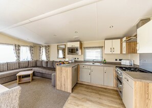 Cocina compacta con microondas, pileta, cocina y alacenas de madera. Cuenta con un espacio de descanso con sofá y una mesa pequeña.