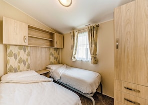 A bedroom with two beds, a wardrobe, and a window with curtains.