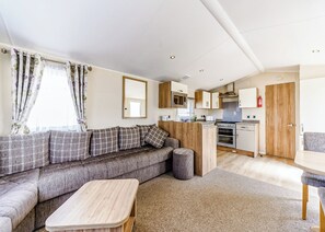 Un espacio habitable compacto con sofá, una mesita de madera, kitchenette y zona de comedor.