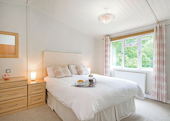 A bedroom with a bed, bedside table, lamp, and window with curtains.