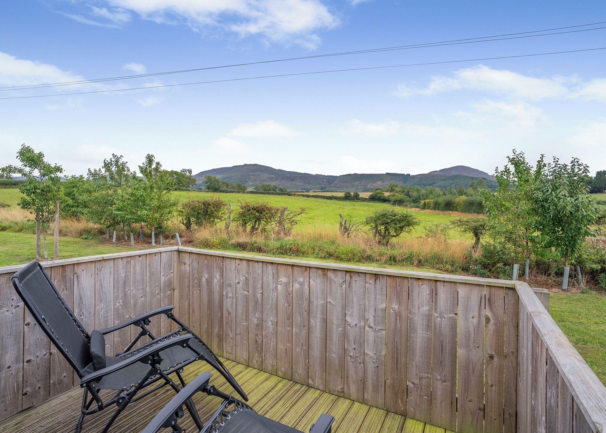 Une terrasse en bois offrant une vue sur un champ verdoyant et des collines.