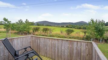 Une terrasse en bois offrant une vue sur un champ verdoyant et des collines.