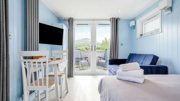 Une chambre avec un lit, un bureau et une chaise, un canapé bleu et une vue sur l’extérieur grâce à une porte vitrée.