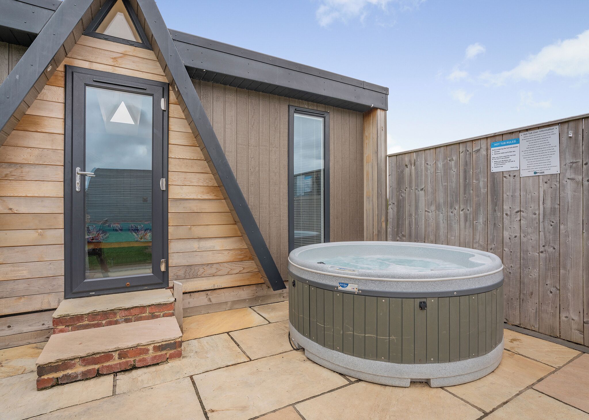 A hot tub outside a wooden building with a metal staircase and a wooden fence.