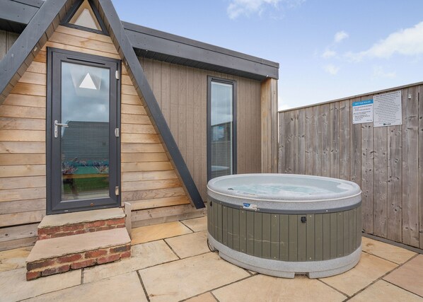 A hot tub outside a wooden building with a metal staircase and a wooden fence.