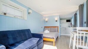Une pièce comprenant un lit, un canapé bleu, une chaise blanche et un coin cuisine.