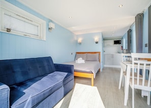 A room with a bed, a blue sofa, a white chair, and a kitchenette. - 1 bedroom accommodation in Great Busby (Great Busby)