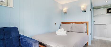 A bedroom with a bed, a chair, a TV, and a kitchenette.